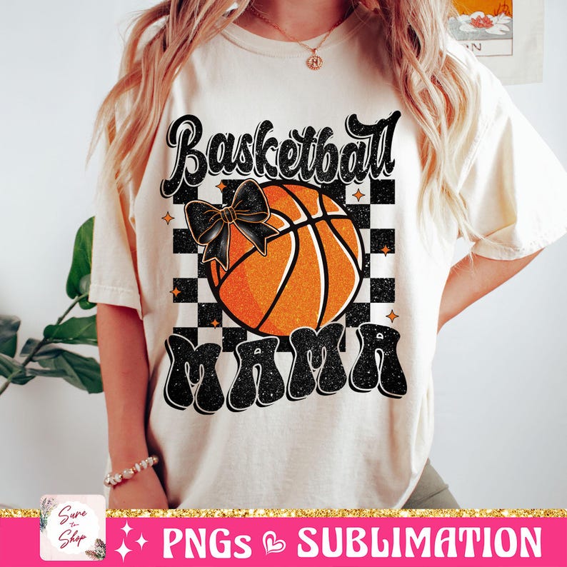 May include: A white t-shirt with a black and orange basketball graphic. The basketball has a black bow on it. The text "Basketball Mama" is written in black with a glittery effect.