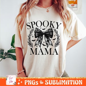 May include: A white t-shirt with the text "Spooky Mama" in black. A black lace bow with bats and stars is centered on the shirt.