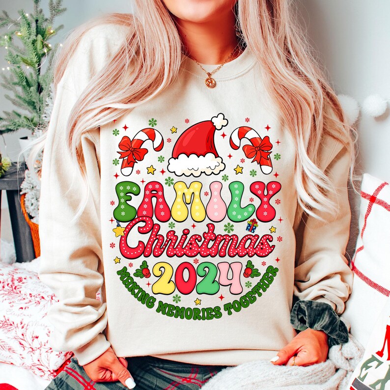 May include: A beige sweatshirt with a colorful graphic design that says "Family Christmas 2024 Making Memories Together". The design features a Santa hat, candy canes, and snowflakes.