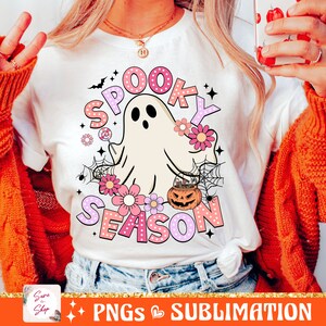 May include: A white t-shirt with a pink and white graphic design that says "Spooky Season" with a ghost, flowers, and a pumpkin.