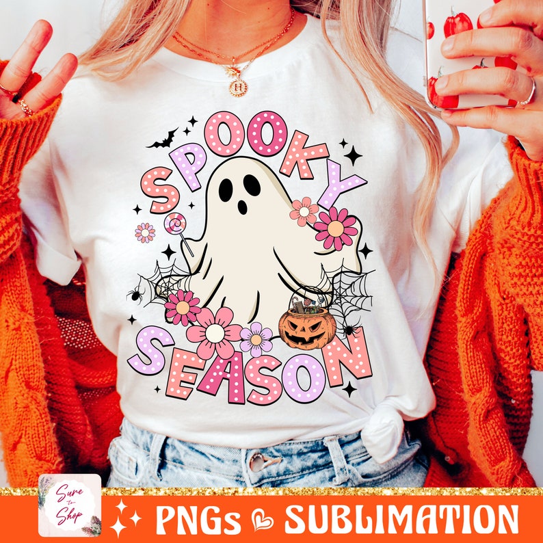 May include: A white t-shirt with a pink and white graphic design that says "Spooky Season" with a ghost, flowers, and a pumpkin.