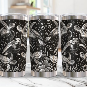 Op de afbeelding: Roestvrijstalen reisbeker met een zwarte achtergrond en een wit zeeschildpadontwerp. Het ontwerp bevat meerdere zeeschildpadden, bellen en waterplanten. De beker heeft een zilveren rand en bodem.