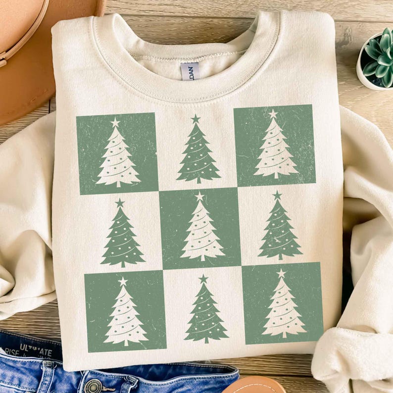 May include: A cream-colored sweatshirt with a green and white Christmas tree design. The trees are arranged in a checkered pattern.