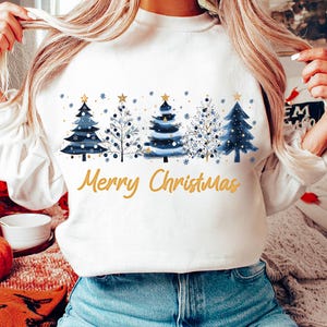 May include: White sweatshirt with a blue and gold Christmas tree design and the text "Merry Christmas".