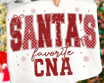 Może przedstawiać: Biała bluza świąteczna z napisem "SANTA'S favorite CNA" w kolorze czerwonym. Litery ozdobione są kropkami i wzorami w kratę. Projekt zawiera płatki śniegu i kokardy.