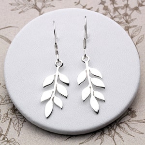 May include: Silver dangle earrings featuring a leaf design. The earrings are made from sterling silver and have a delicate, feminine look.