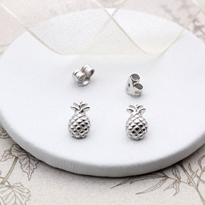 May include: A pair of silver pineapple stud earrings. The earrings are small and delicate, and they would make a great gift for someone who loves pineapples.