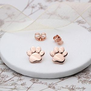 May include: A pair of rose gold paw print stud earrings. The earrings are small and delicate, and they would make a great gift for any dog lover.