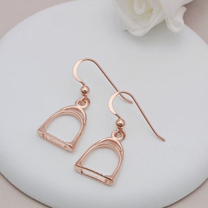May include: A pair of rose gold stirrup earrings. The earrings are made of metal and have a simple, elegant design.
