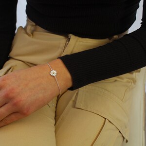 Puede incluir: Un brazalete de cadena de plata con un delicado encanto de margarita blanca.