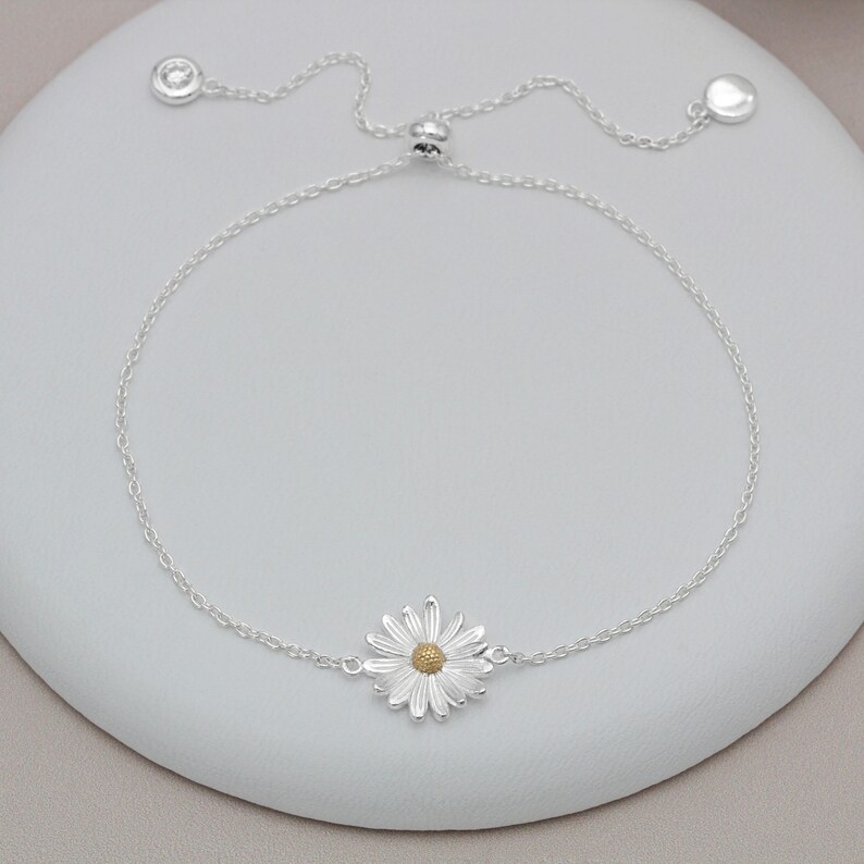 Puede incluir: Un brazalete de cadena de plata con un delicado encanto de margarita. El brazalete tiene un cierre deslizante para un tama&ntilde;o ajustable.