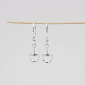 Puede incluir: Pendientes de aro de plata con un dije de bocado de caballo de plata que cuelga de cada aro.