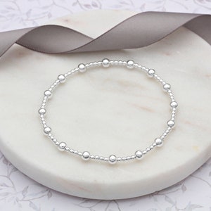 May include: A silver beaded bracelet with small, evenly spaced beads. The bracelet is on a white marble surface.