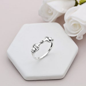 May include: A silver ring with a simple, elegant design featuring a horse bit motif. The ring is shown on a white background.