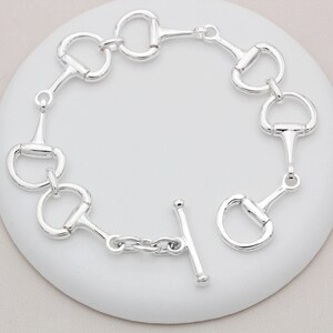 May include: Silver bracelet with a chain link and multiple silver horse bit charms. The bracelet has a t-bar clasp.
