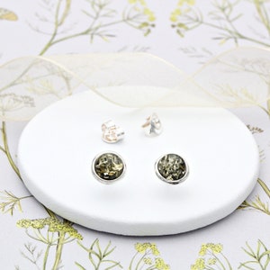 May include: A pair of silver stud earrings with green amber stones. The earrings are on a white surface.
