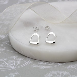 Puede incluir: Un par de pendientes de plata en forma de estribo. Los pendientes tienen un acabado liso y pulido.