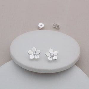 Könnte beinhalten: Ein Paar silberne Blumenohrstecker mit einem kleinen, klaren Strassstein in der Mitte jeder Blume.