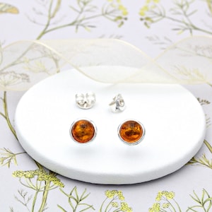 May include: A pair of silver stud earrings with round amber stones. The earrings are on a white surface.
