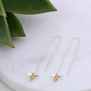 May include: A pair of silver chain earrings with a gold bee charm at the end of each chain.
