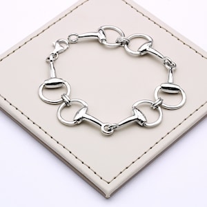May include: A silver bracelet with a chain made of interlocking horse bit links.