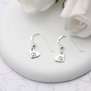 May include: A pair of silver dangle earrings with a heart-shaped charm featuring a paw print cutout.