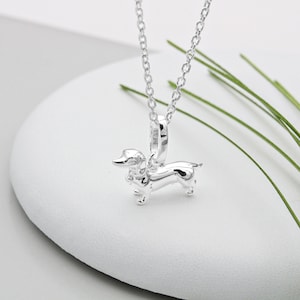 May include: A silver necklace featuring a small, detailed dachshund charm. The charm hangs from a delicate silver chain.