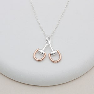 May include: A silver chain necklace with a double-sided pendant featuring two silver and rose gold horse bit charms.