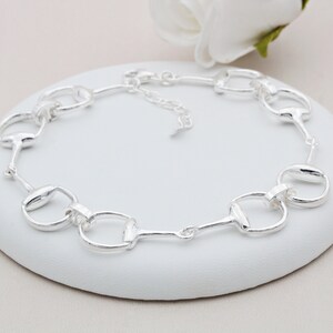May include: A silver bracelet with a chain link design featuring multiple interlocking horse bit charms.