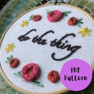 May include: Embroidered hoop art featuring the phrase "to the thing" in brown thread. The hoop is decorated with pink and orange flowers and green leaves.