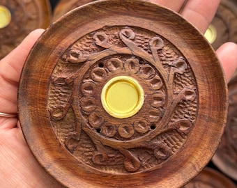 May include: A round wooden incense burner with a carved floral design and a gold metal center. The burner is held in a hand.