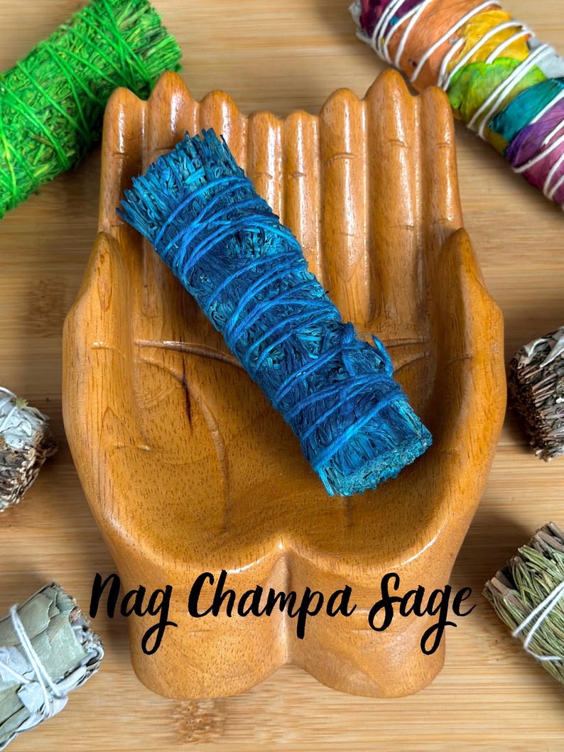 May include: A blue sage bundle wrapped in string resting in a carved wooden hand-shaped dish. The text Nag Champa Sage is centered below the bundle. Other sage bundles in green, rainbow, and natural tones are visible in the corners.