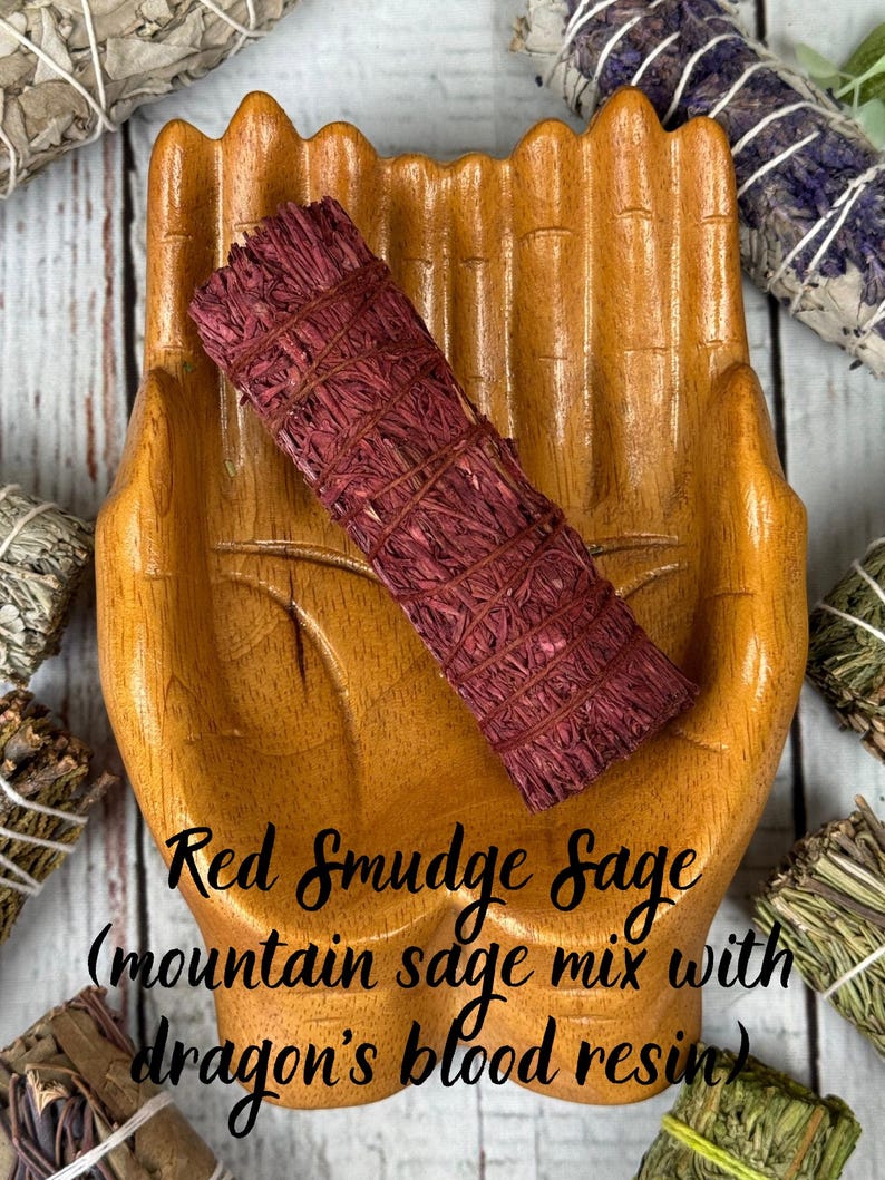May include: A cylindrical bundle of red smudge sage tied with thin string, resting in a carved wooden hand-shaped dish. The text on the image reads: Red Smudge Sage (mountain sage mix with dragon's blood resin).