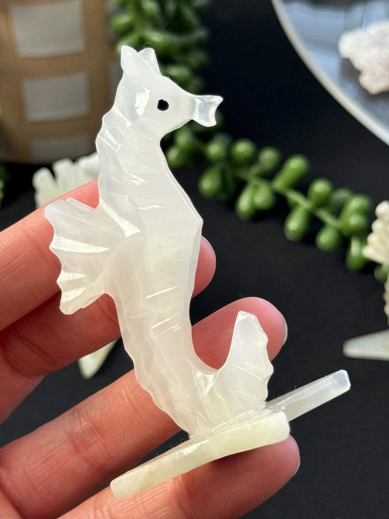 Puede incluir: Figurita de caballito de mar tallada en blanco con un dise&ntilde;o detallado. El caballito de mar est&aacute; de pie sobre una base blanca.