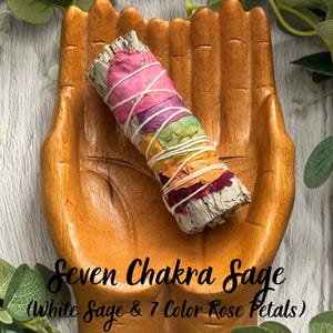 May include: A wooden hand-shaped dish holding a sage smudge stick wrapped in white string, decorated with seven layers of colored rose petals. The text Seven Chakra Sage (White Sage & 7 Color Rose Petals) is printed over the image.