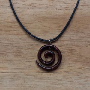 May include: A dark brown wooden spiral pendant necklace on a black cord.