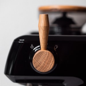 May include: A black espresso machine with a wooden knob and a chrome portafilter. The machine has a silver lever on the side.