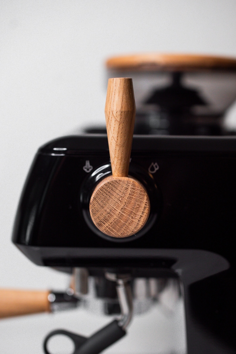 May include: A black espresso machine with a wooden knob and a chrome portafilter. The machine has a silver lever on the side.