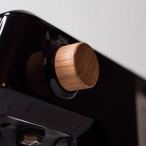 May include: Close-up of a black espresso machine with a wooden knob. The knob is labeled "Steam".