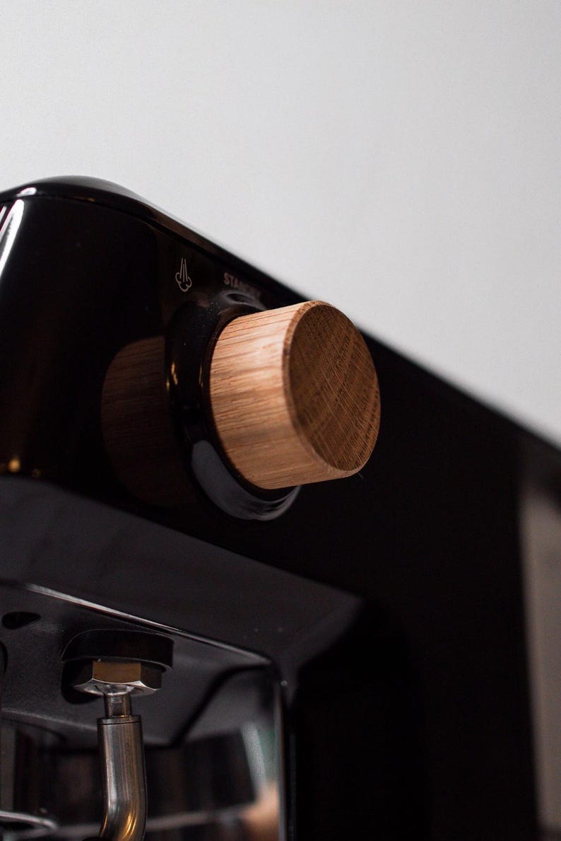 May include: Close-up of a black espresso machine with a wooden knob. The knob is labeled "Steam".
