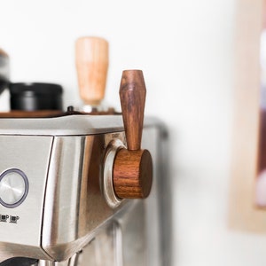 May include: A close-up of a silver espresso machine with a wooden handle. The handle is labeled "Steam".