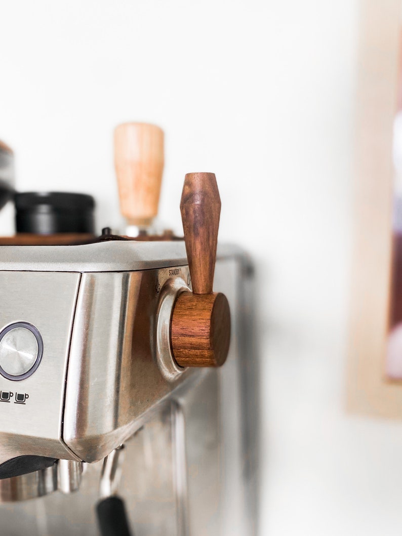 May include: A close-up of a silver espresso machine with a wooden handle. The handle is labeled "Steam".