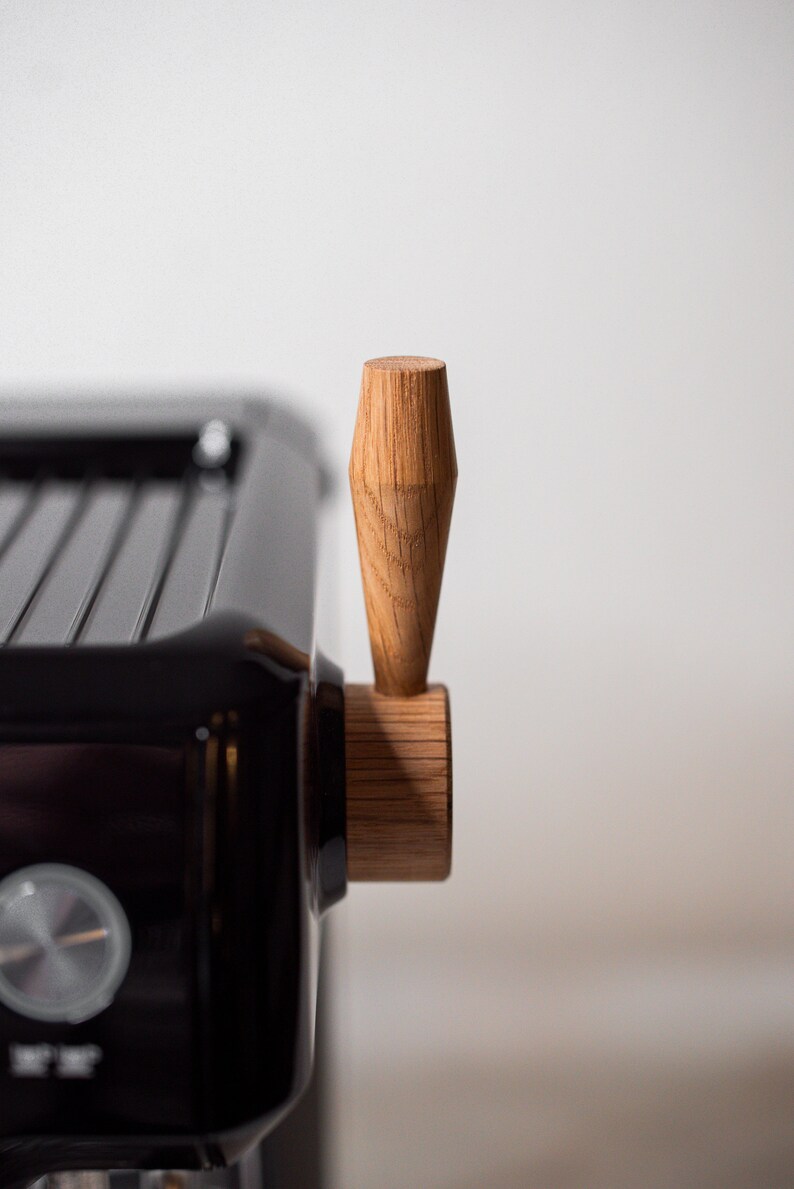 May include: Close-up of a black espresso machine with a wooden handle. The handle is a light brown color and has a slightly rounded shape.