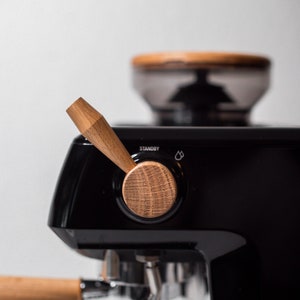 May include: A black espresso machine with a wooden handle and knob. The machine has a grinder on top and a portafilter with a wooden handle.