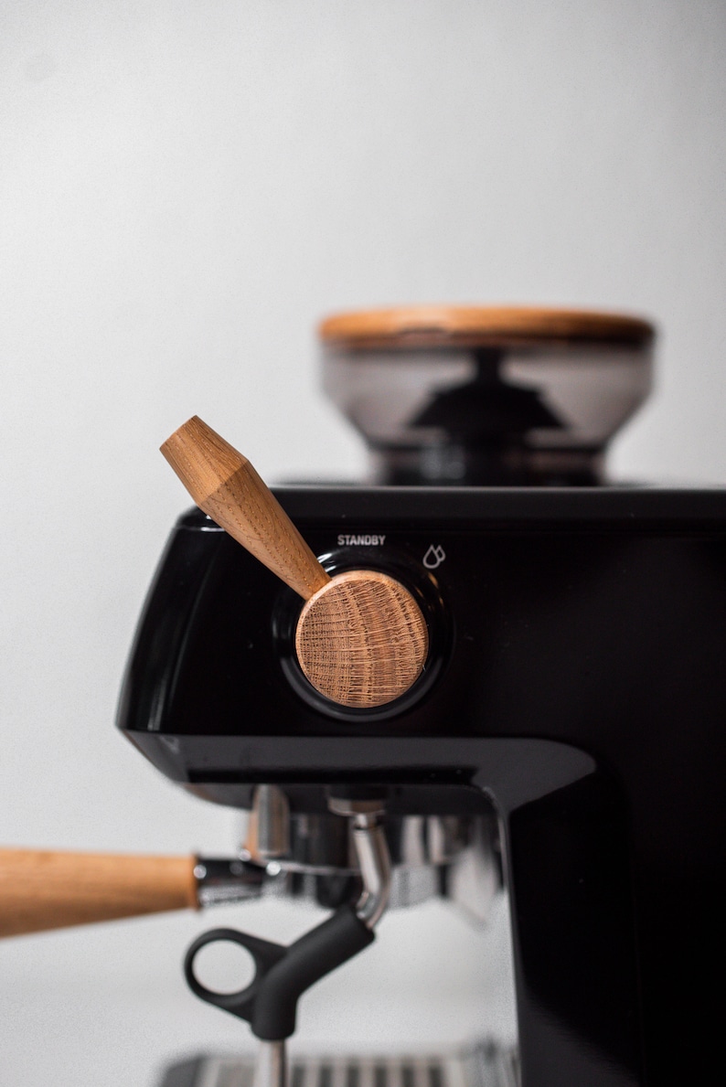 May include: A black espresso machine with a wooden handle and knob. The machine has a grinder on top and a portafilter with a wooden handle.