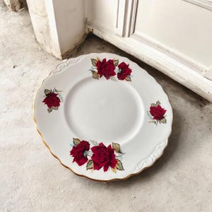 Può includere: Piatto in ceramica bianca con bordo smerlato e finiture dorate. Il piatto è decorato con grappoli di rose rosse e foglie verdi. Un pezzo decorativo per servire cibo o per l'esposizione.
