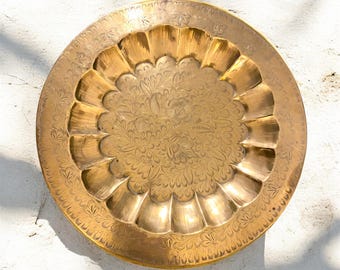May include: A round, brass tray with an intricate floral design. The tray has a scalloped edge and a raised center.