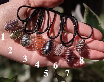 May include: Eight crystal cage pendants with different colored stones. The pendants are on black cords and are numbered 1 through 8. The stones are amethyst, green aventurine, white, carnelian, black, rose quartz, and red jasper.