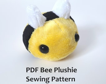 Pode incluir: Um brinquedo de pelúcia de abelha amarelo e preto com asas brancas. A abelha tem olhos pretos grandes e uma pequena boca preta. O brinquedo de pelúcia é um padrão de costura.