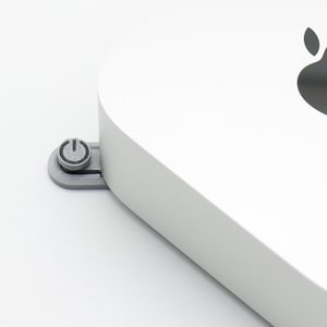 Könnte beinhalten: Ein weißer Apple Mac mini Computer mit einem schwarzen Apple-Logo auf der Oberseite. Der Netzschalter befindet sich an der Seite des Geräts.